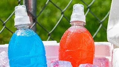Two plastic sports drink bottles, one blue and one orange, with white caps, chilling in an ice-filled cooler.