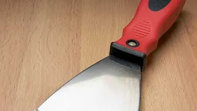 Putty knife with a red and black handle on a wooden surface.