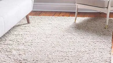 White shag rug on hardwood floor between two light-colored furniture pieces.