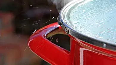 Steam and boiling water escaping from under the lid of a red pot.