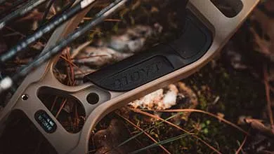 Close-up of a black grip on a tan Hoyt compound bow lying on the forest floor.