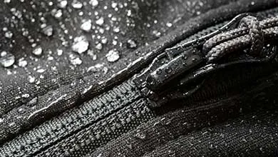 Close-up of a black fabric zipper covered with water droplets, demonstrating moisture resistance and surface performance.