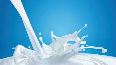 White milk pours down, forming a crown-shaped splash on a bright blue background.