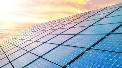 Low-angle view of large solar panels reflecting orange light from sunrise or sunset.