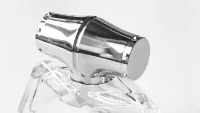Close-up of a shiny silver metal cap with small studs and a flared shape on a clear glass bottle, set against a white background.